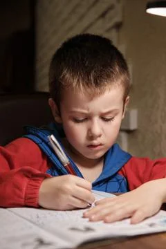 Child Is Doing Homework In The Light Of The Lamp In The Evening. A Boy Sits a Stock Photos