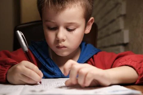 Child Is Doing Homework In The Light Of The Lamp In The Evening. A Boy Sits a Stock Photos