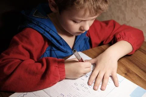 Child Is Doing Homework In The Light Of The Lamp In The Evening. A Boy Sits a Stock Photos