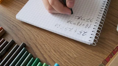 Child doing math exercises in notebook with stationery on wooden table. Girl Video stock 283763694