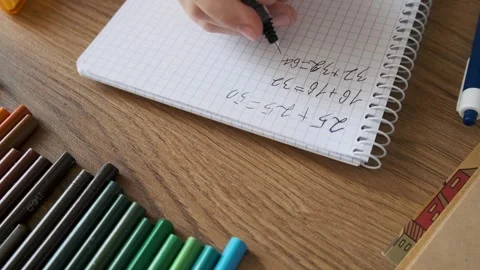 Child doing math exercises in notebook with stationery on wooden table. Girl Stock Footage 284931341