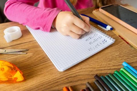 Child doing math exercises in notebook using smartphone with stationery on Stock Photos