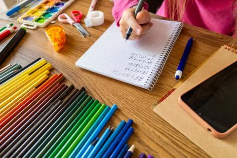 Child doing math test in notebook using smartphone with stationery on wooden Stock Photos