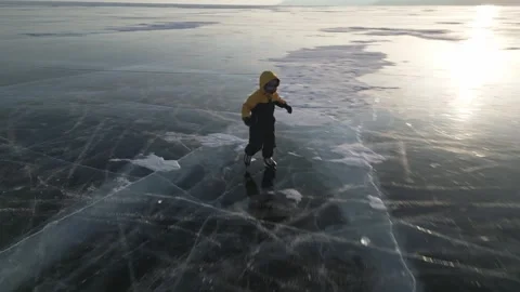 A child in a down jacket is clumsily skating on the winter Lake Baikal Stock Footage 278020637