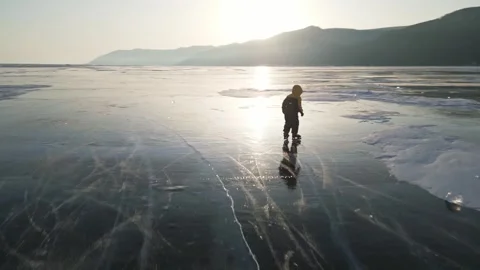 A child in a down jacket is clumsily skating on the winter Lake Baikal Stock Footage 278020765