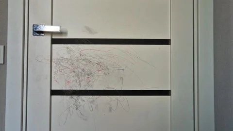 Child drawing with crayons on a white interior door, messy scribbles on wall sur Video stock 332985949