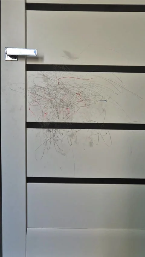 Child drawing with crayons on a white interior door, messy scribbles on wall sur Video stock 332985951