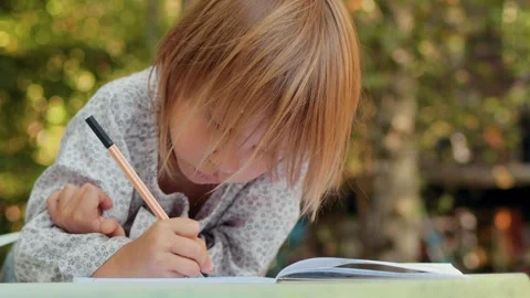 Child drawing with fineliners in notebook in a summer garden Stock Footage 304328550