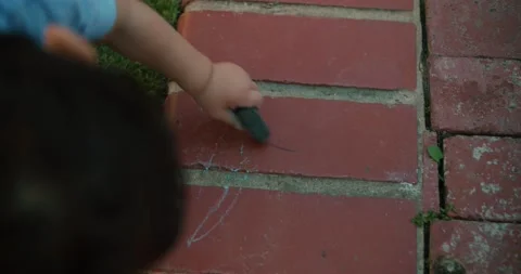 Child drawing on ground with chalk overhead Stockbeeldmateriaal 174083152