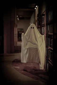 Child dressed as a white ghost in a library room Stock Photos