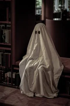Child dressed as a white ghost in a library room Stock Photos
