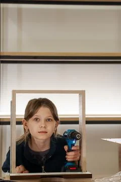Child drilling into frame with serious expression in workshop Stock Photos