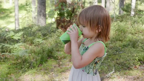 Child drinking from a green cup in a forest setting Stock Footage 293002669