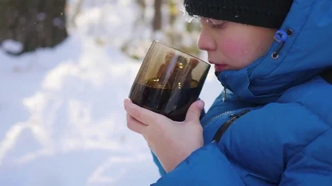 The child is drinking hot tea from a mug in the winter outdoor. Sunny day 库存影片 69096410