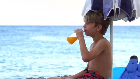 Child Drinking Orange Juice on the Beach Vidéo 79905424