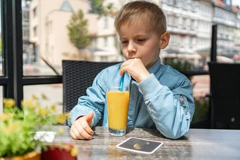 Child Drinking Orange Juice While Sitting at a Table Fotos de archivo