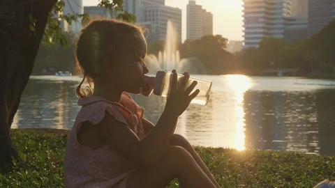 Child drinking water at the park with lake and skyscrapers on the background Stock Footage 88903353