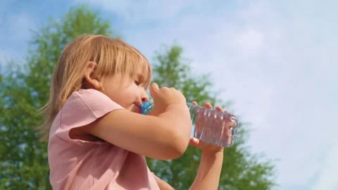 Child drinking water from a plastic bottle on a sunny day outdoors Video stock 295218325