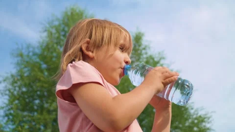 Child drinking water from a plastic bottle on a sunny day outdoors Stock Footage 295218343