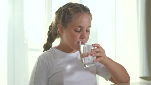 Child drinking water at table. Child holding glass of water sitting at table 库存影片 315904264