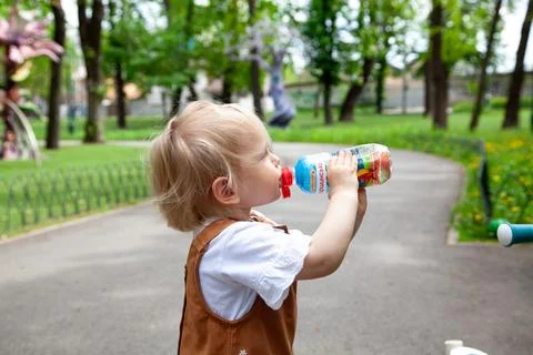 Child drinks from bottle while playing in park on a sunny day Generative AI Photos