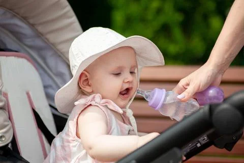 Child drinks from bottle while sitting in stroller outside during sunny day Stock Photos