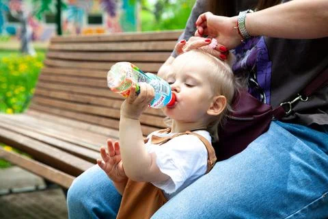 Child drinks from a bottle while sitting on a bench in a park on a sunny da.. Stock Photos