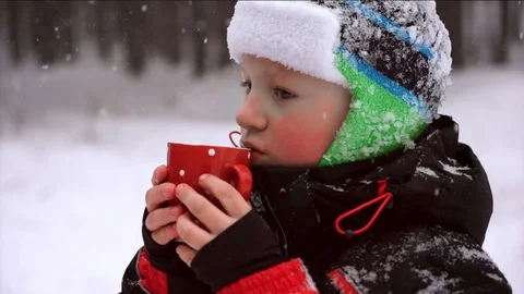 The child drinks a hot drink in the winter forest, the snow lies, it's snowing Video stock 88921483