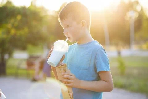 A child drinks a milkshake and eats a hotdog outdoors in a park Stock Photos