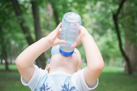 A child drinks water from a bottle while walking, baby health concept Stock Photos