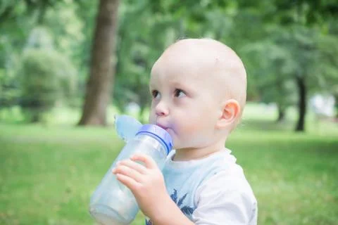 A child drinks water from a bottle while walking, baby health concept Stock Photos
