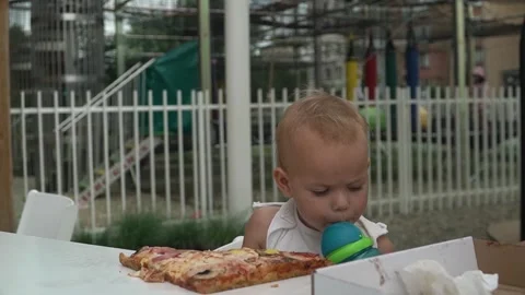 Child drinks water sippy cup through straw while eating pizza cafes summer Stock Footage 317345752