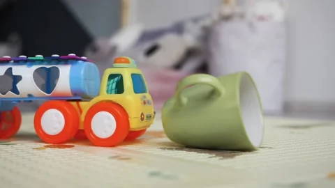 A child drops a small machine, pours tea from a mug on the carpet in the room Stock Footage 142213897