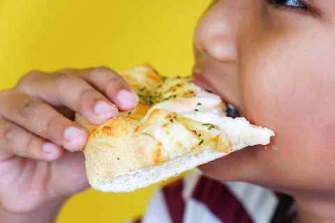 A child eagerly bites into a cheesy slice of pizza, enjoying a delicious mo.. Stock Photos