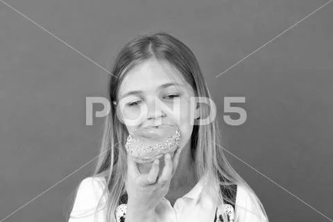 Child eat donut on violet background. Little girl bite glazed ring doughnut Stock Photos