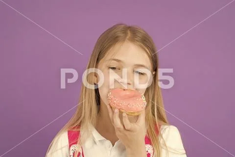 Child eat donut on violet background. Little girl bite glazed ring doughnut Stock Photos