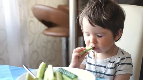 Child eating sliced cucumbers at the table of the house Stock Footage 134944257