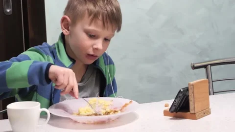 The child eats and looks at the phone Stock Footage 148320520
