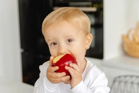 The child eats an apple for breakfast sitting in the kitchen. Healthy eating for Photos