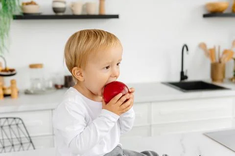 The child eats an apple for breakfast sitting in the kitchen. Healthy eating for 写真素材