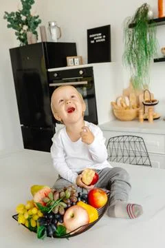 The child eats an apple for breakfast sitting in the kitchen. Healthy eating for 库存照片
