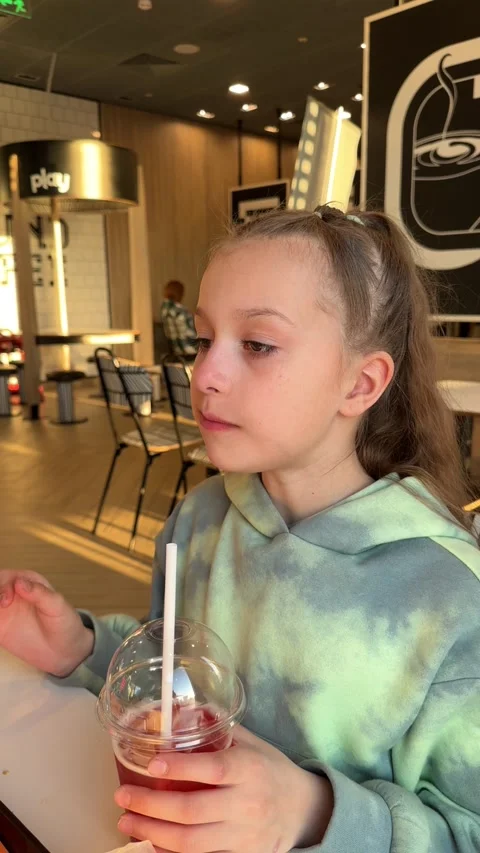 The child eats a big burger in a fast food restaurant, unhealthy food, the girl Stock Footage 241080343