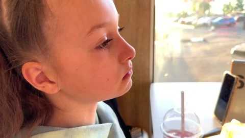 The child eats a big burger in a fast food restaurant, unhealthy food, the girl Stock Footage 241080417