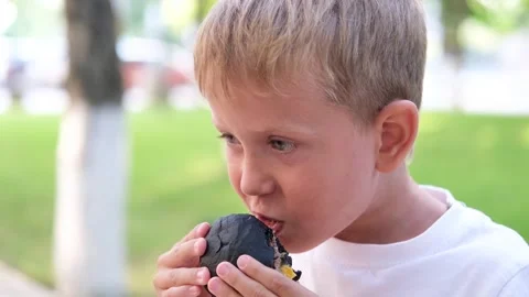The child eats a black burger on the street. Stock Footage 248607873
