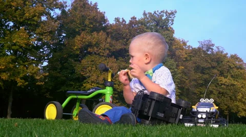 The Child Eats Bread, Sitting in the Park on the Grass Among Toys Stock Footage 68101927