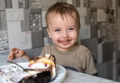 The child eats a cake and shows emotions. 스톡 사진