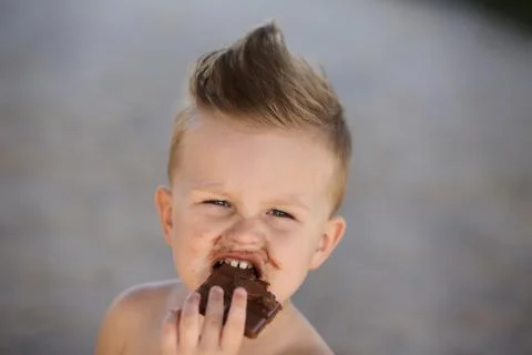 Child eats chokolate with full stength on a beach Stock Photos