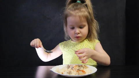 Child eats cooked rice and mushrooms with a spoon on a black background at the Stock Footage 111332782