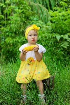 The child eats the corn in nature. Funny little girl eats in the Park. Stock Photos