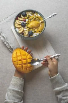 The child eats fruit. Children's hands hold a spoon and half a mango, next to a Stock Photos